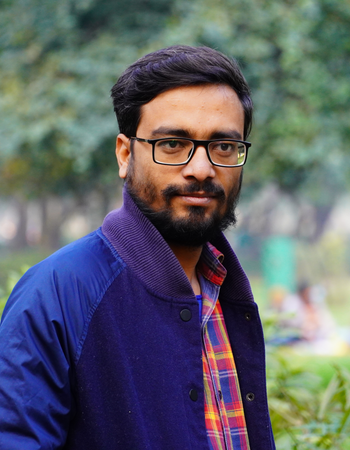 Man wearing glasses and a blue jacket with a plaid shirt in a park setting